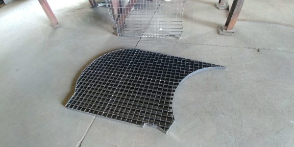 A close-up view of a grid metal plate lying on a concrete floor, showcasing its curved edge and wire mesh design.
