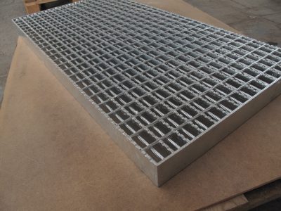 Close-up of a metal grating panel resting on a wooden surface, showcasing its structured grid design and metallic finish.